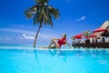 Elegant sexy woman in the red bikini on the sun-tanned slim and shapely body is posing near the swimming pool on Maldives. Perfect Royalty Free Stock Photo