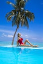 Elegant sexy woman in the red bikini on the sun-tanned slim and shapely body is posing near the swimming pool on Maldives. Perfect Royalty Free Stock Photo