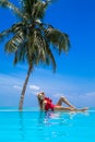 Elegant sexy woman in the red bikini on the sun-tanned slim and shapely body is posing near the swimming pool on Maldives. Perfect Royalty Free Stock Photo