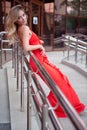 An elegant sexy woman in a tight red dress poses leaning against the railing of a street staircase in summer Royalty Free Stock Photo