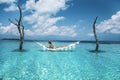 Elegant sexy woman in the white bikini on the sun-tanned slim and shapely body is posing on hammock in ocean on Maldives. Perfect Royalty Free Stock Photo