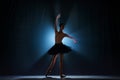 Elegant silhouette of elegant young girl, ballet dancer dancing on stage against dark blue background with spotlight