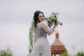 Elegant and smiling bridesmaid holding bridal bouquett in front of the church and posing for camera