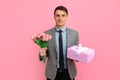 Elegant smiling man with gift box and bouquet of flowers over pink background Concept for Valentine\'s Day Royalty Free Stock Photo
