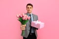 Elegant smiling man with gift box and bouquet of flowers  over pink background  Concept for Valentine\'s Day Royalty Free Stock Photo