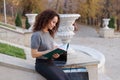 Elegant smiling woman with curly hair working at laptop and makes notes in agend. Business woman working outside.