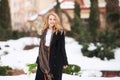 Elegant smiling young woman with long blonde hair in a black coat poses in the city. Portrait of a beautiful modern woman with Royalty Free Stock Photo