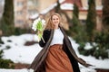 Elegant smiling young woman with long blonde hair in a black coat poses in the city. Portrait of a beautiful modern woman with Royalty Free Stock Photo