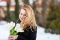 Elegant smiling young woman with long blonde hair in a black coat poses in the city. Portrait of a beautiful modern woman with Royalty Free Stock Photo