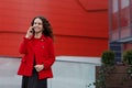 Elegant smiling young woman in red, talking on the smartphone walking outside. Cheerful woman using mobile.