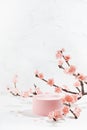 Elegant spring cylinder podium mockup with branch of pink sakura flowers in light white interior on table in japanese style