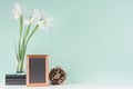 Elegant spring interior with fresh white flowers, black books, blank wood photo frame, decorative round sheaf of brown twigs.