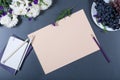 Elegant still life - sheet of beige paper, white and purple chrysanthemums, pencils, notebooks and plate with grapes on gray back