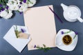 Elegant still life - sheet of paper, white and purple chrysanthemums, pencil, teapot, cup of herbal tea and envelope on gray desk Royalty Free Stock Photo