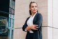 Elegant stylish lady stands in a black austere suit leaning on the wall of the business center