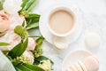 Elegant sweet dessert macarons, cup of coffee and pastel colored beige flowers bouquet on white marble Royalty Free Stock Photo