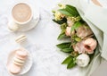 Elegant sweet dessert macarons, cup of coffee and pastel colored beige flowers bouquet on white marble Royalty Free Stock Photo