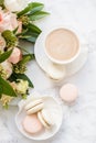 Elegant sweet dessert macarons, cup of coffee and pastel colored beige flowers bouquet on white marble Royalty Free Stock Photo