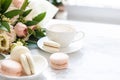 Elegant sweet dessert macarons, cup of coffee and pastel colored beige flowers bouquet on white marble Royalty Free Stock Photo