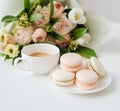 Elegant sweet dessert macarons, cup of coffee and pastel colored beige flowers bouquet Royalty Free Stock Photo