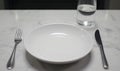 Elegant Table Setting: Empty Plate, Fork, Knife, and Water Glass on Marble Surface Royalty Free Stock Photo