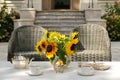 Elegant tea serving in garden with sunflowers in vase on marble table with silver tea pot and cookies