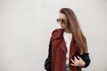 Elegant urban young hipster woman in stylish dark sunglasses in fashionable brown trench coat walks on the city near vintage wall Royalty Free Stock Photo