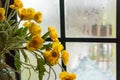An elegant vase of yellow flowers next to the glass window still has dewdrops. Romantic floral decoration Royalty Free Stock Photo