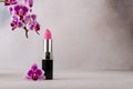 An elegant vibrant pink lipstick beside a beautiful purple orchid flower Royalty Free Stock Photo