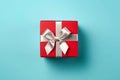 Vibrant red gift box decorated with white satin ribbon and bow, against a pastel blue backdrop Royalty Free Stock Photo