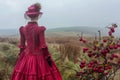 Elegant Victorian Lady in Red Dress Contemplating Nature on a Misty Countryside Morning Royalty Free Stock Photo