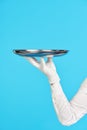 Elegant waiter& x27;s hand in white glove holding metal tray on blue background. Royalty Free Stock Photo