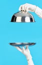 Elegant waiter& x27;s hands in white gloves holding silver tray and cloche on blue background Royalty Free Stock Photo