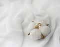 Elegant wedding concept. Golden ring with cotton flower pillow on white silk background.