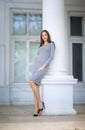 An elegant woman on the background of a large white house. The beautiful lady in a gray dress and black shoes outdoors Royalty Free Stock Photo