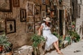 Elegant woman donning a pristine white dress and a hat relaxing in a picturesque alleyway