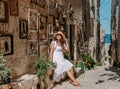 Elegant woman donning a pristine white dress and a hat relaxing in a picturesque alleyway