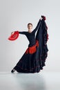 Elegant woman, flamenco dancer with fan in hand, black and red dress performing against grey studio background