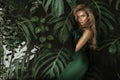 Elegant woman in a green evening dress poses sensually against the background of Monstera plants Royalty Free Stock Photo