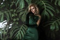 Elegant woman in a green evening dress poses sensually against the background of Monstera plants Royalty Free Stock Photo