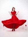 elegant woman in a long flittering red dress is standing in a white room