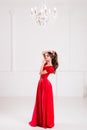 Elegant woman in a long red dress is standing in a bright room w