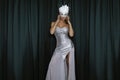 Elegant Woman is wearing Carnival Feather Mask and sequin silver evening dress and is posing on dark velvet background. Masquerade Royalty Free Stock Photo