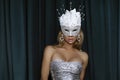 Elegant Woman is wearing Carnival Feather Mask and sequin silver evening dress and is posing on dark velvet background. Masquerade Royalty Free Stock Photo