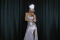 Elegant Woman is wearing Carnival Feather Mask and sequin silver evening dress and is posing on dark velvet background. Masquerade Royalty Free Stock Photo