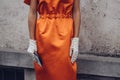 Elegant woman wearing orange long dress, black bag and white gloves