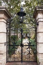 Elegant wrought iron alley gate with decorative leaves and rosettes topped by gaz lamp