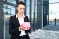 Elegant young beautiful businesswoman holds a piggy bank on the background of the entrance of a business center building Royalty Free Stock Photo