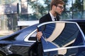 Elegant young businessman entering his car while standing outdoors