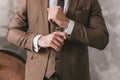 Elegant young fashion man looking at his cufflinks while fixing them. Photo of male hands. Handsome groom dressed in brown formal Royalty Free Stock Photo